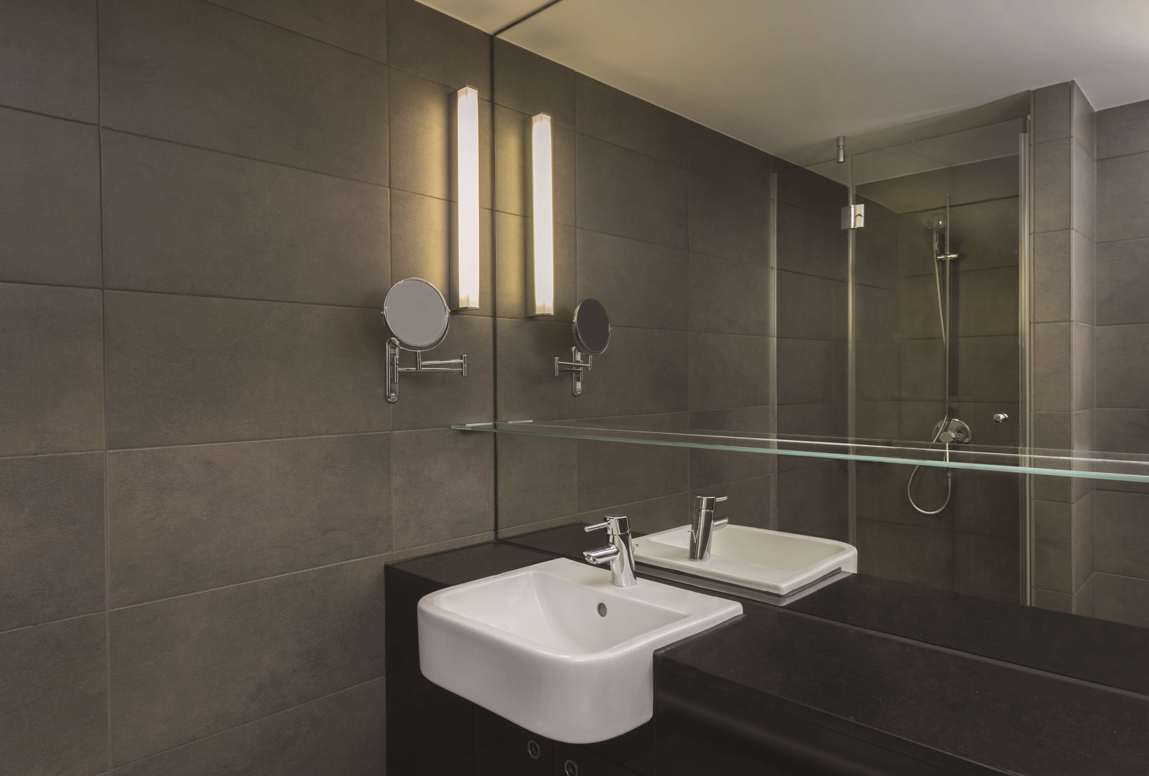 Une salle de bain moderne avec un grand miroir, deux vasques et une douche à l’italienne.