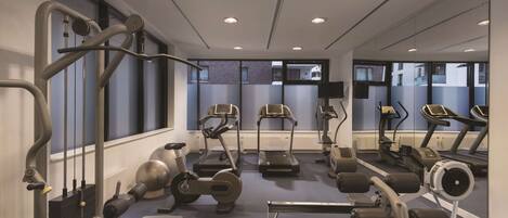 A gym with various exercise equipment, large windows, and a mirrored wall.