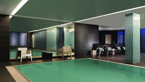 A modern indoor swimming pool with a glass barrier, seating area, and a lounge with chairs and tables. - Adina Apartment Hotel Hamburg Michel (Hamburg)