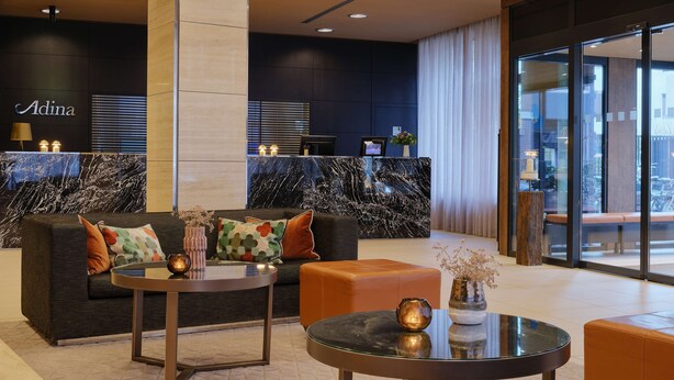 A modern lobby with a marble reception desk, a sofa with colorful cushions, a glass coffee table, and a seating area with a leather ottoman. - Adina Apartment Hotel Hamburg Michel (Hamburg)