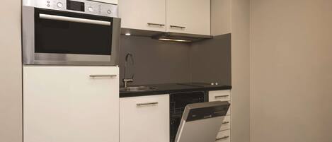 Una cocina compacta con gabinetes blancos, horno de acero inoxidable, lavavajillas y encimera negra.