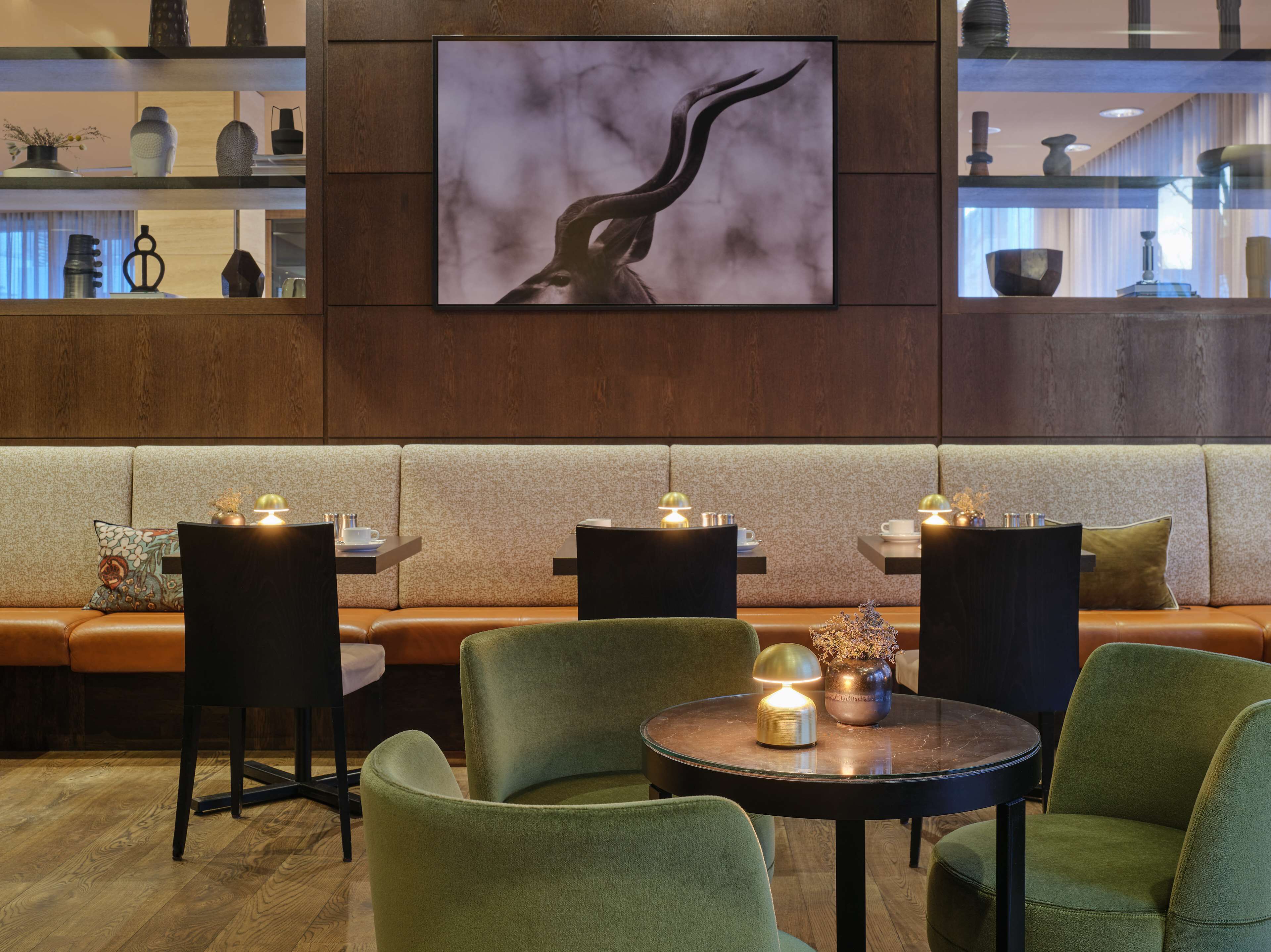 Ein moderner Lounge-Bereich mit einer Couch, drei grünen Sesseln und einem runden Tisch mit einer Lampe.