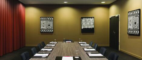 Un salón de conferencias con una larga mesa, sillas negras y decoración en la pared.