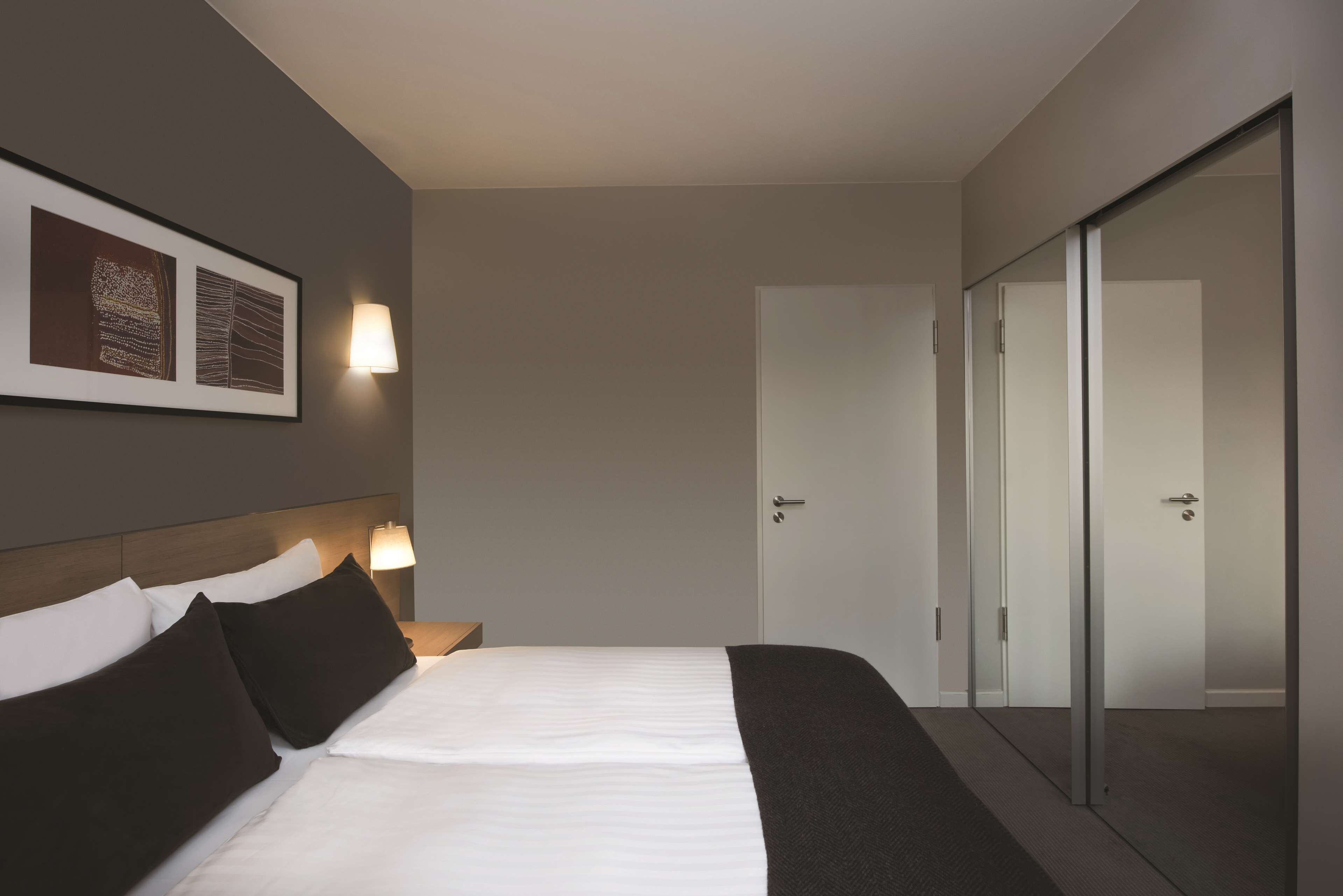 A hotel room with a bed, two bedside lamps, a framed artwork on the wall, and a sliding door closet.