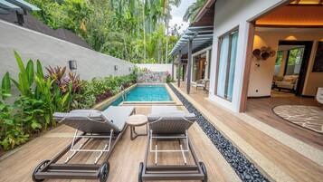 A modern outdoor pool area with two lounge chairs, a small table, and a stone wall.