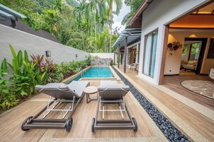 A modern outdoor pool area with two lounge chairs, a small table, and a stone wall.