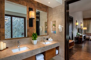 A modern bathroom with a large mirror, two sinks, a potted plant, and a towel rack.