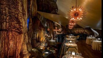 An interior with tables set for dining, a chandelier, and a large rock formation.