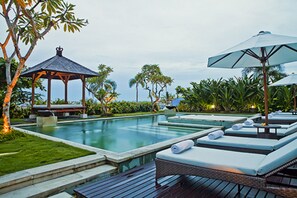 Un espace aménagé au bord de la piscine, avec des chaises longues, un kiosque et une vue sur l’océan.
