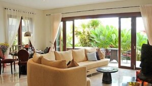 A spacious living area with a beige sofa, a coffee table, and a view of lush greenery through large sliding glass doors.