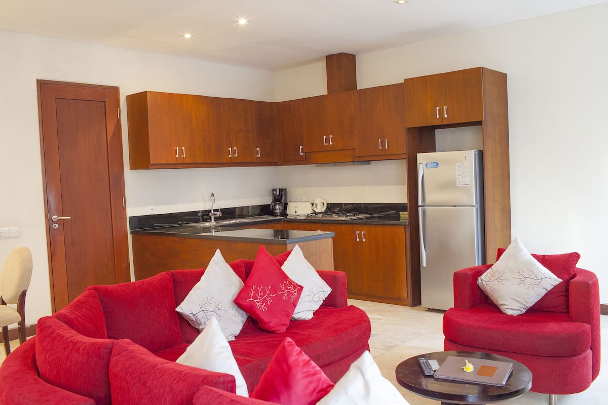 A modern kitchen with wooden cabinets, a refrigerator, and a dining area with a red sofa and a coffee table.
