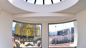 Una habitación con tragaluces y dos ventanas que ofrecen vistas a arquitectura histórica.
