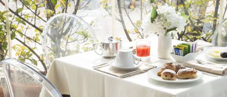 A breakfast table with a white tablecloth, a pitcher, a cup, a glass of juice, a plate with pastries, and a vase with flowers.