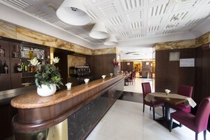 Una hall d'hotel moderna con una reception in marmo, un'area bar e un'area ristorazione con sedie rosse e un tavolo.