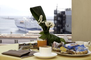 Una colazione con vista su una nave da crociera, una tazza di caffè, un bicchiere di succo, un piatto con pasticcini e un vaso con fiori.