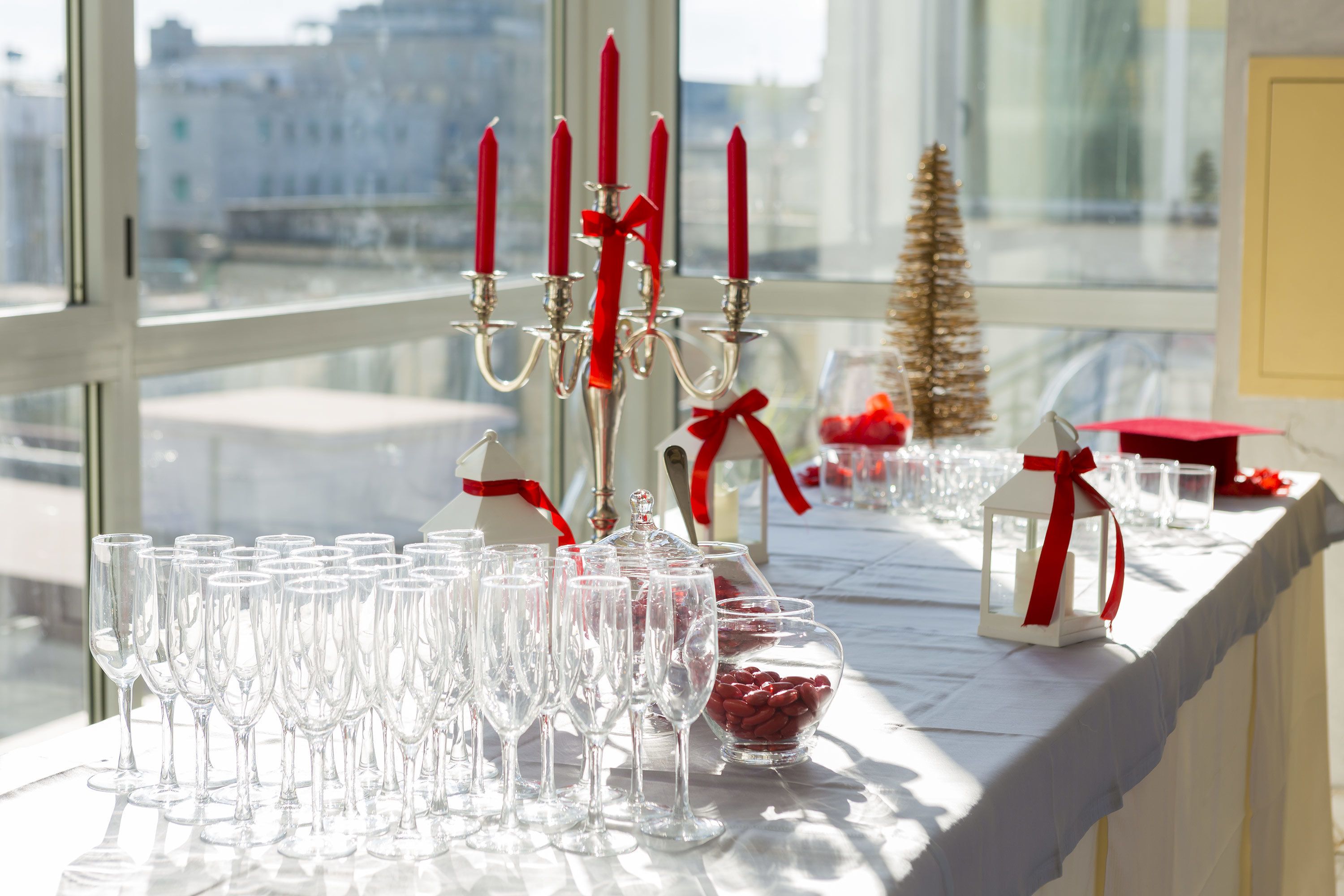 A table set with clear glasses, a candelabra with red candles, and a small Christmas tree.