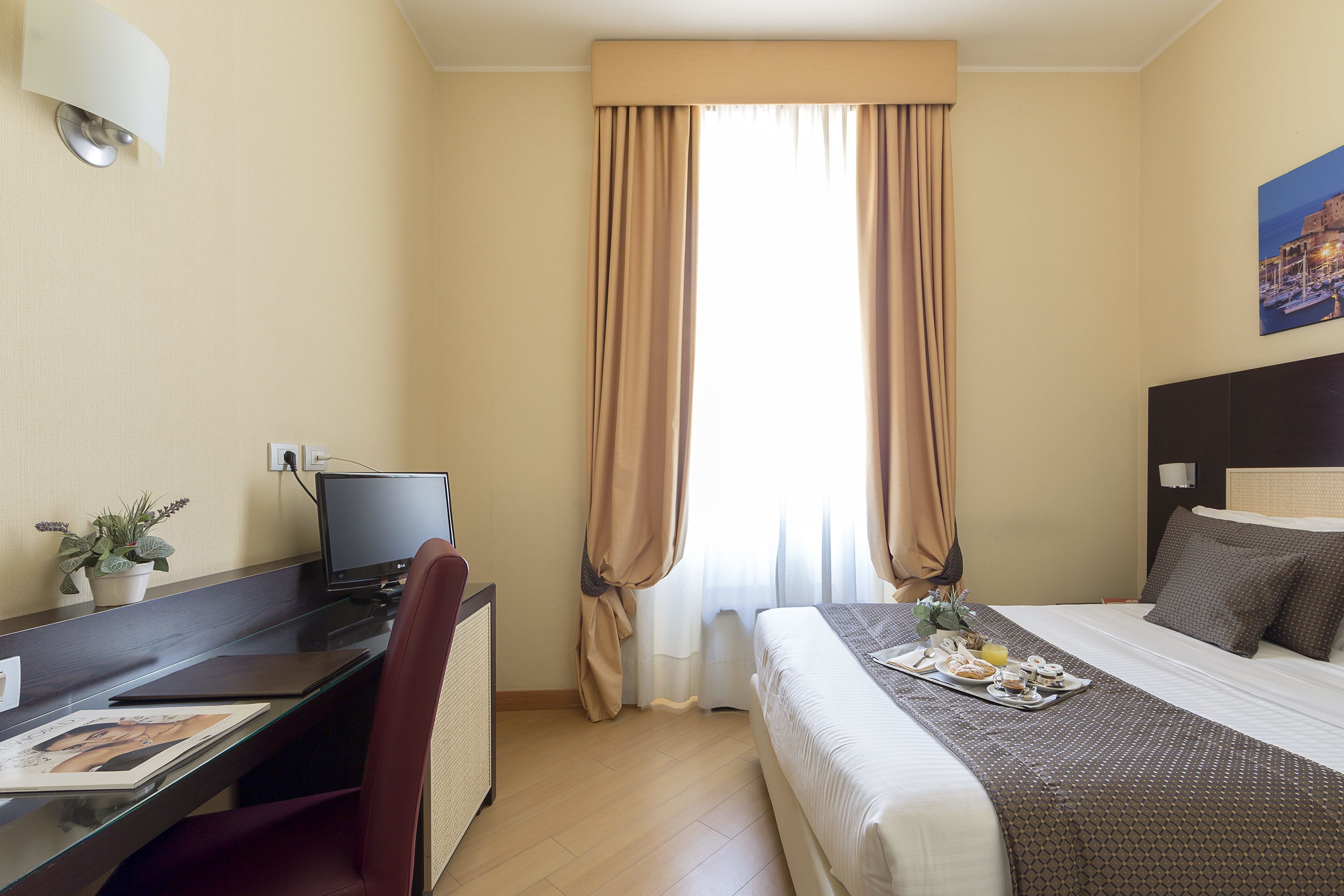 A hotel room with a bed, desk, and computer.