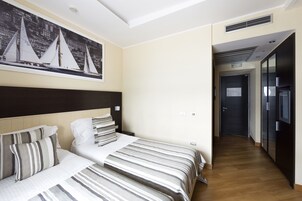 Una camera d'albergo con un letto grande, una testiera, un quadro appeso al muro raffigurante dei velieri e un pavimento in legno.