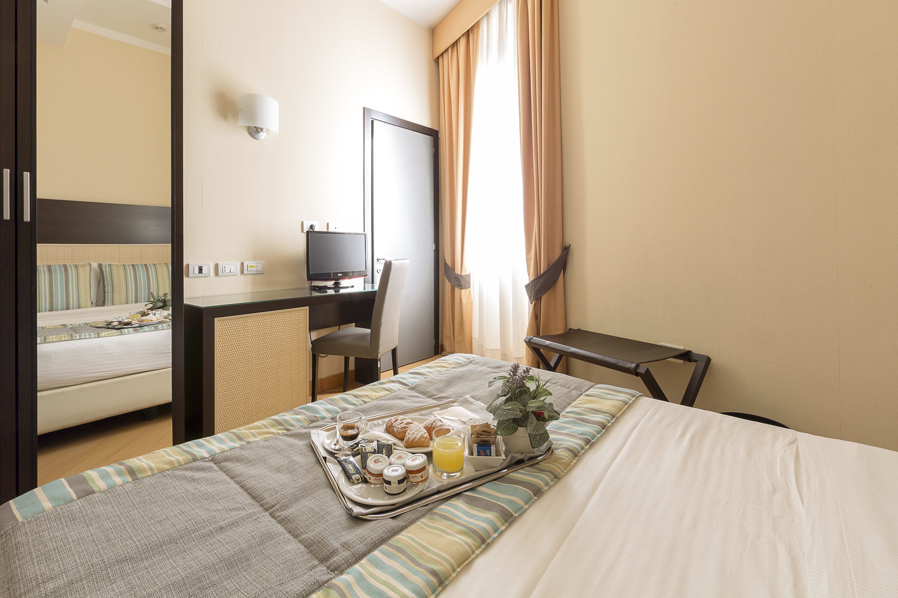 Habitación de hotel con cama, escritorio, silla y bandeja con productos para el desayuno.