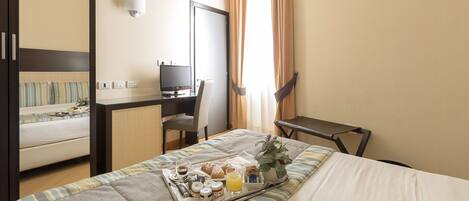 Habitación de hotel con cama, escritorio, silla y bandeja con productos para el desayuno.