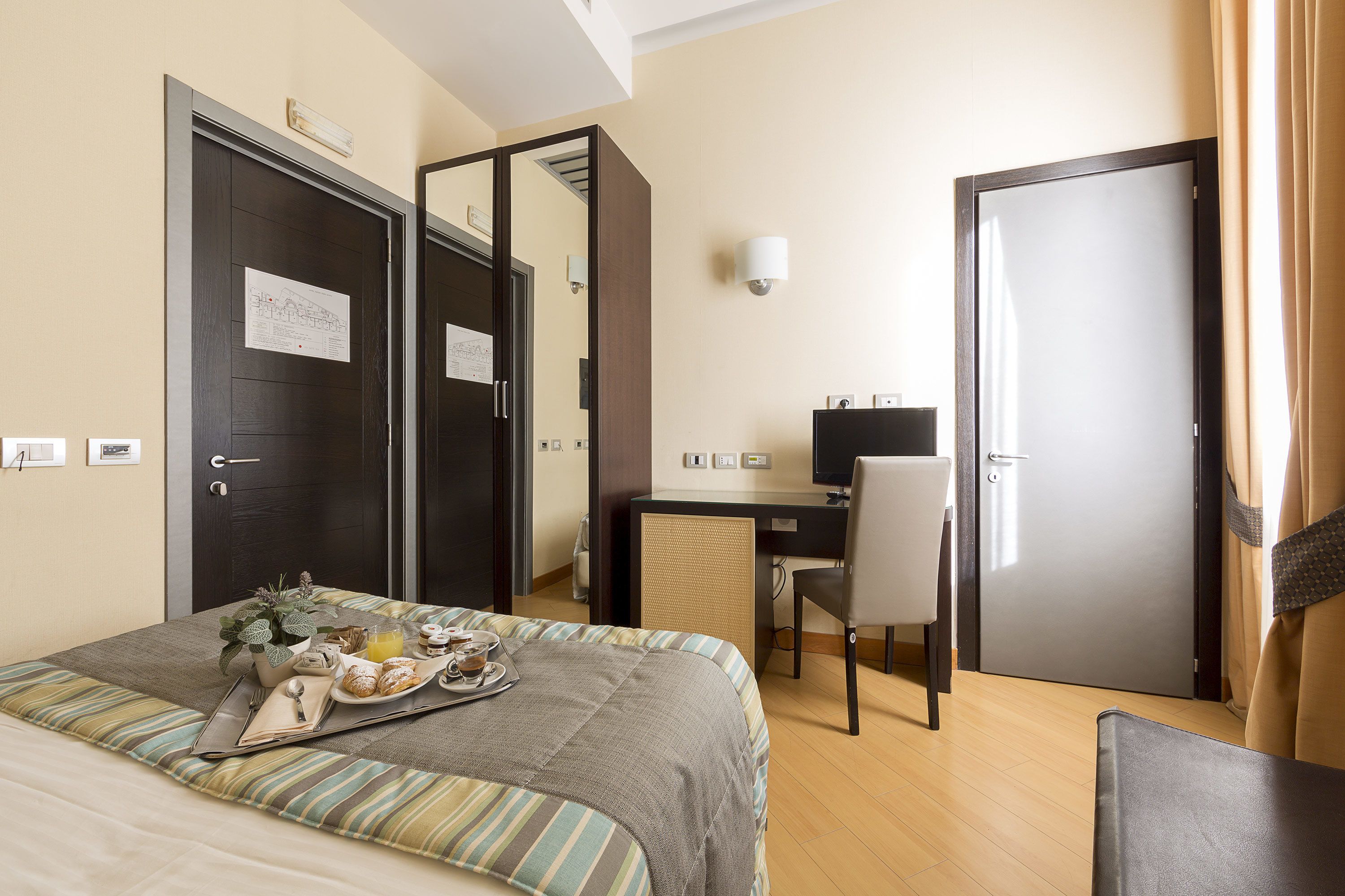 Una camera d'albergo con un letto, una scrivania con un computer, una sedia e una porta.