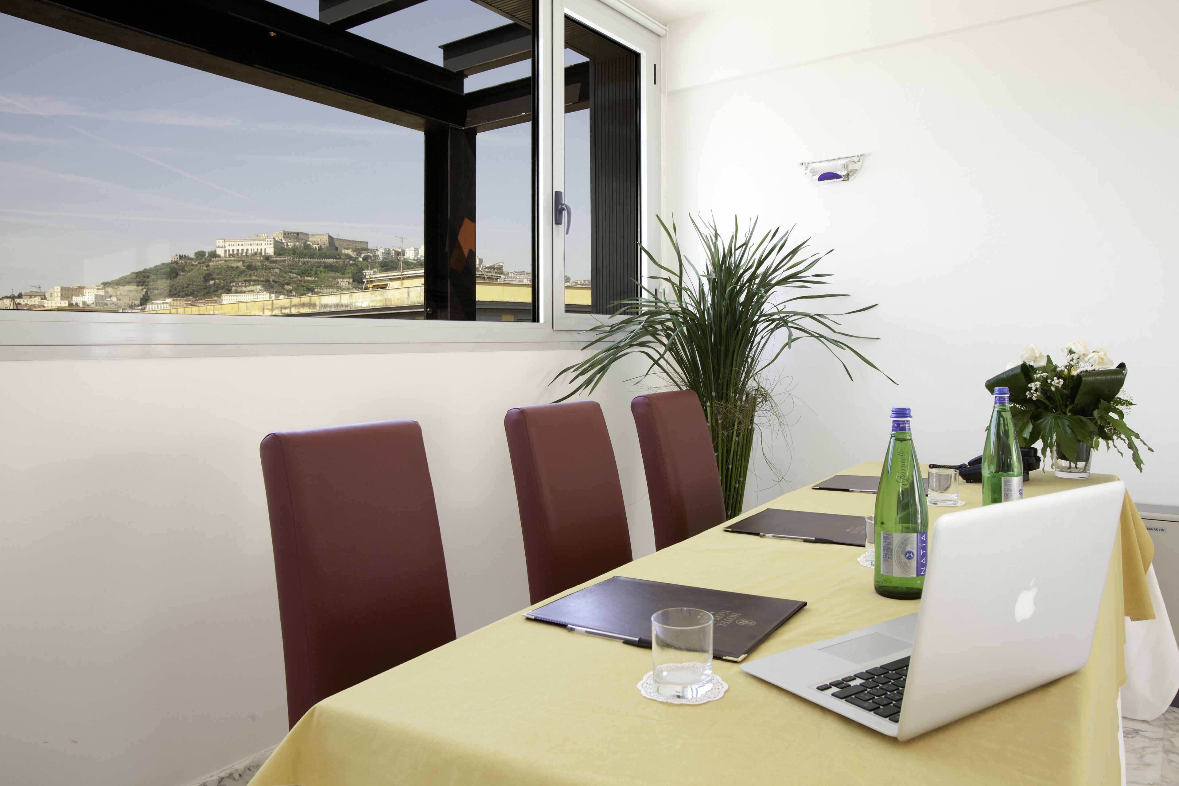 Une salle de conférence équipée d’une table, de chaises, d’un ordinateur portable et offrant une vue sur une colline parsemée de bâtiments.