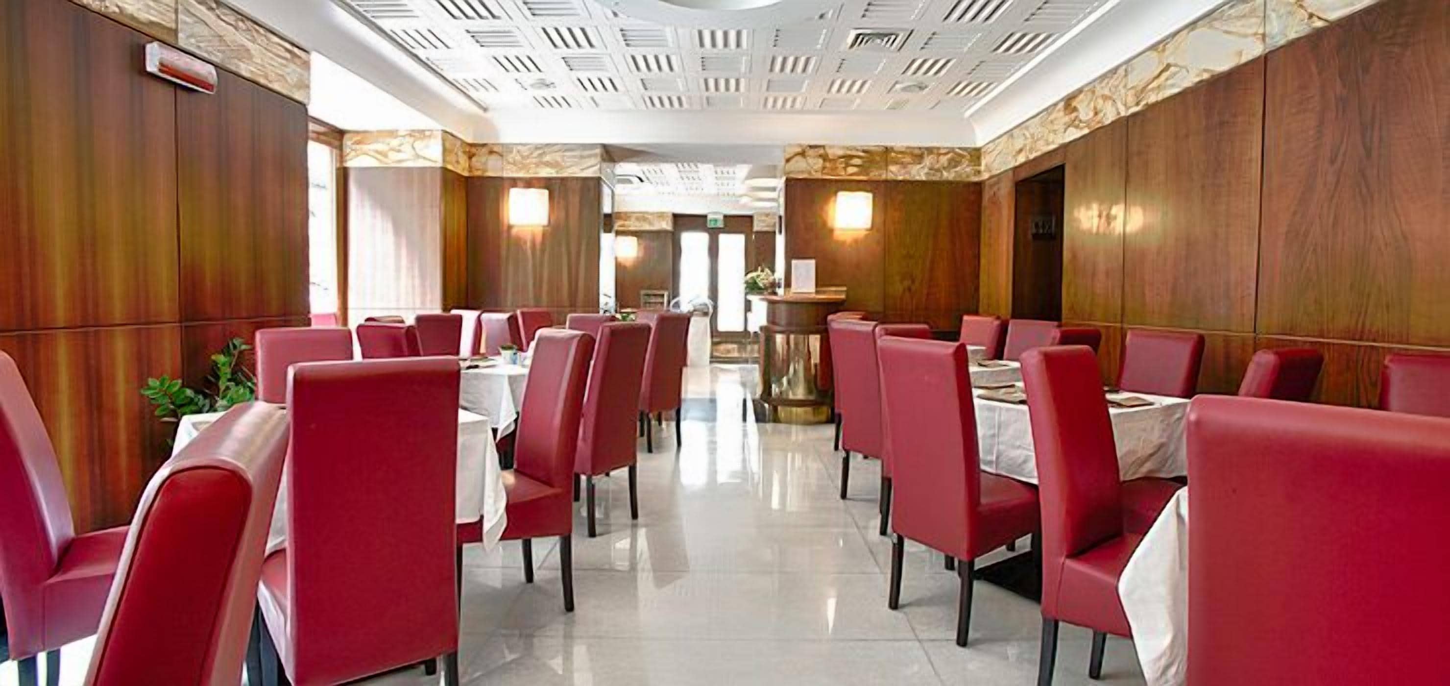 En restaurant med røde stole, hvide duge, en sleben gulv og et dekorativt loft.