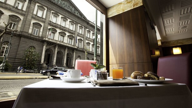 Una mesa de comedor con alimentos para el desayuno, vista por la ventana a un edificio histórico y una calle de la ciudad.