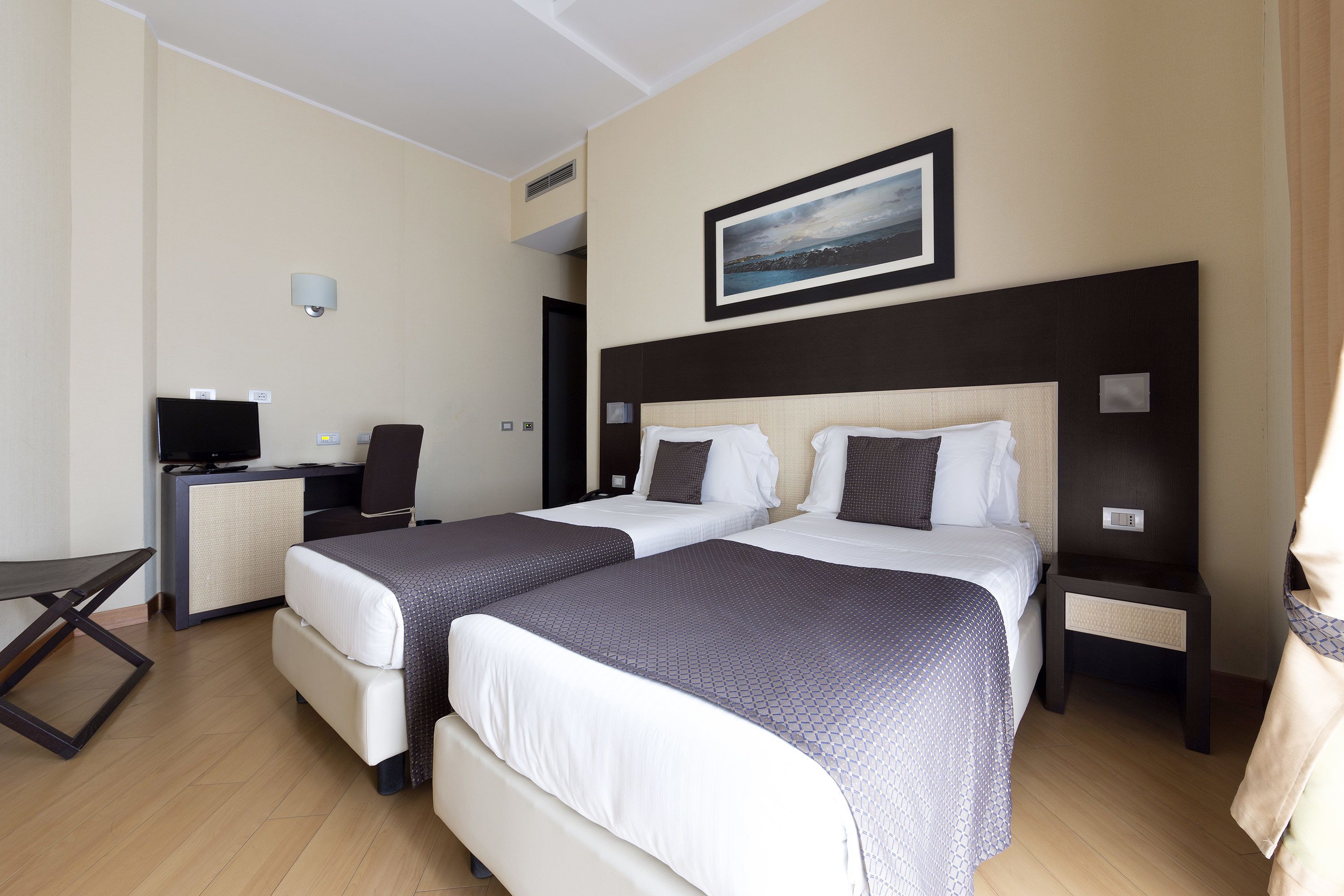 A hotel room with two beds, a desk, a chair, and a TV.