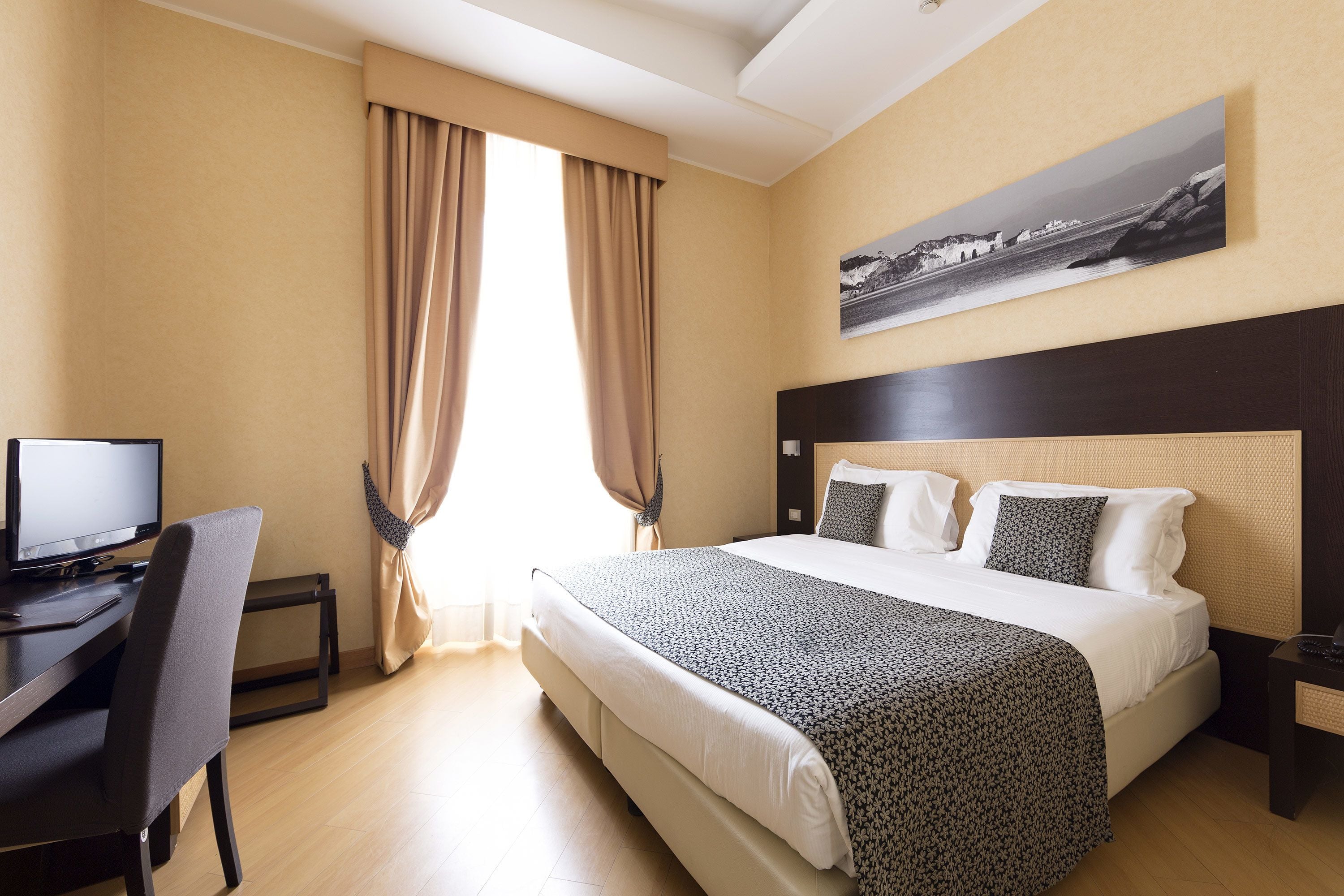 Una camera d'albergo con un letto, una scrivania e un computer.
