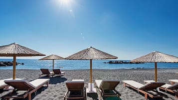 Am Strand, schwarzer Sandstrand, Liegestühle, Sonnenschirme