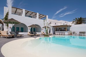A poolside area with lounge chairs, a bar, and a building with arched windows. - Nissia Beach Apartments and Suites (Santorini)