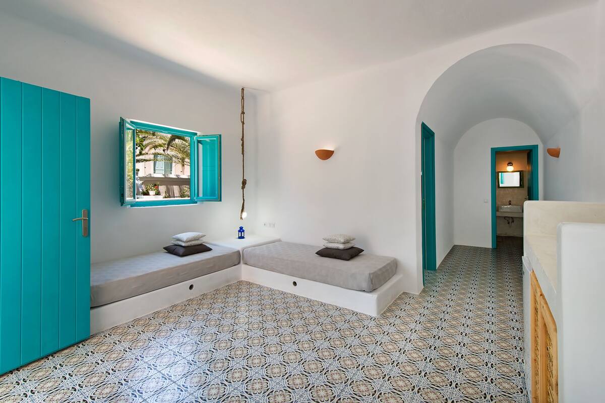 A room with a white and turquoise color scheme, featuring a bench with pillows, a wall-mounted mirror, and patterned flooring.