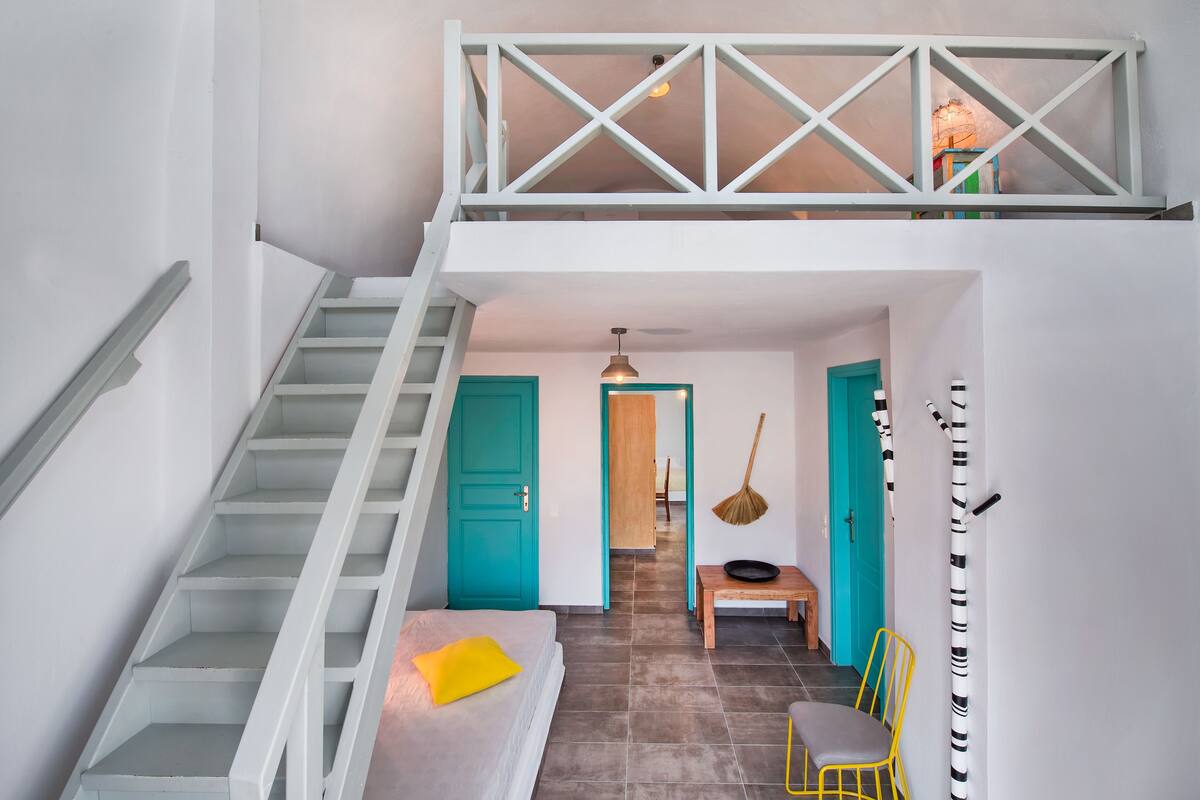 A staircase leading to a loft area with a bed, a chair, and a dining table.