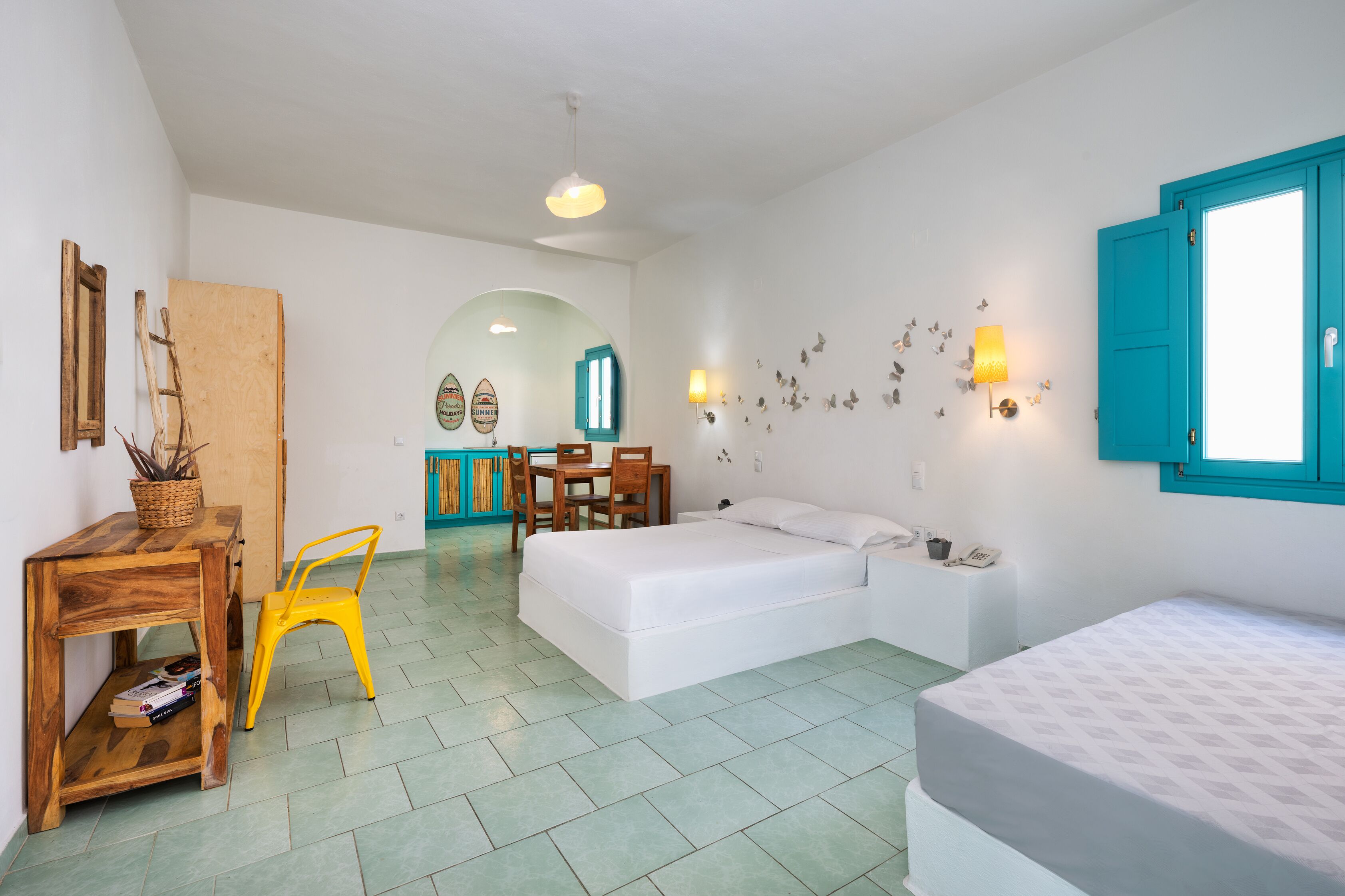 A room with a bed, a desk, a chair, a table, and a wall with a window and wall art.