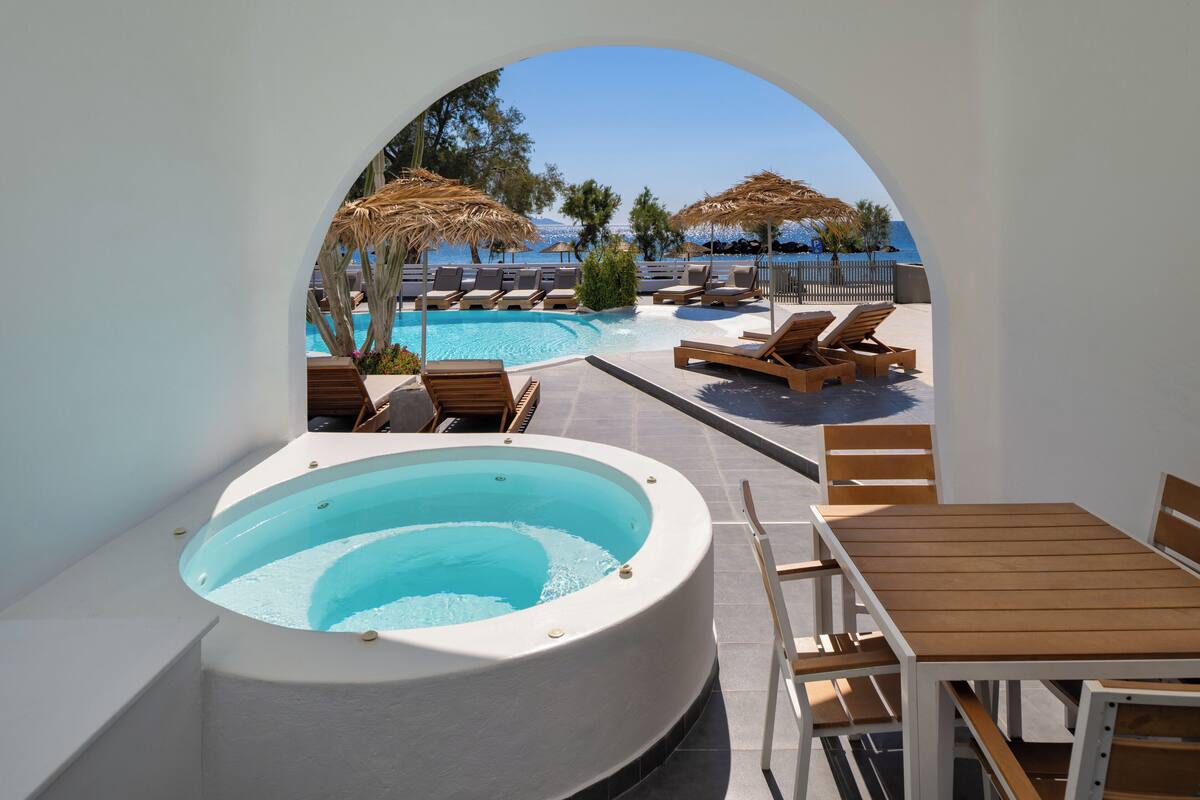 A pool area with a hot tub, lounge chairs, and umbrellas.