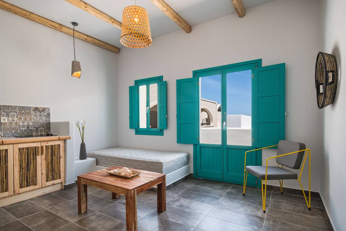 A modern living room with a wooden table, a sofa, teal doors, and a view of a white building.