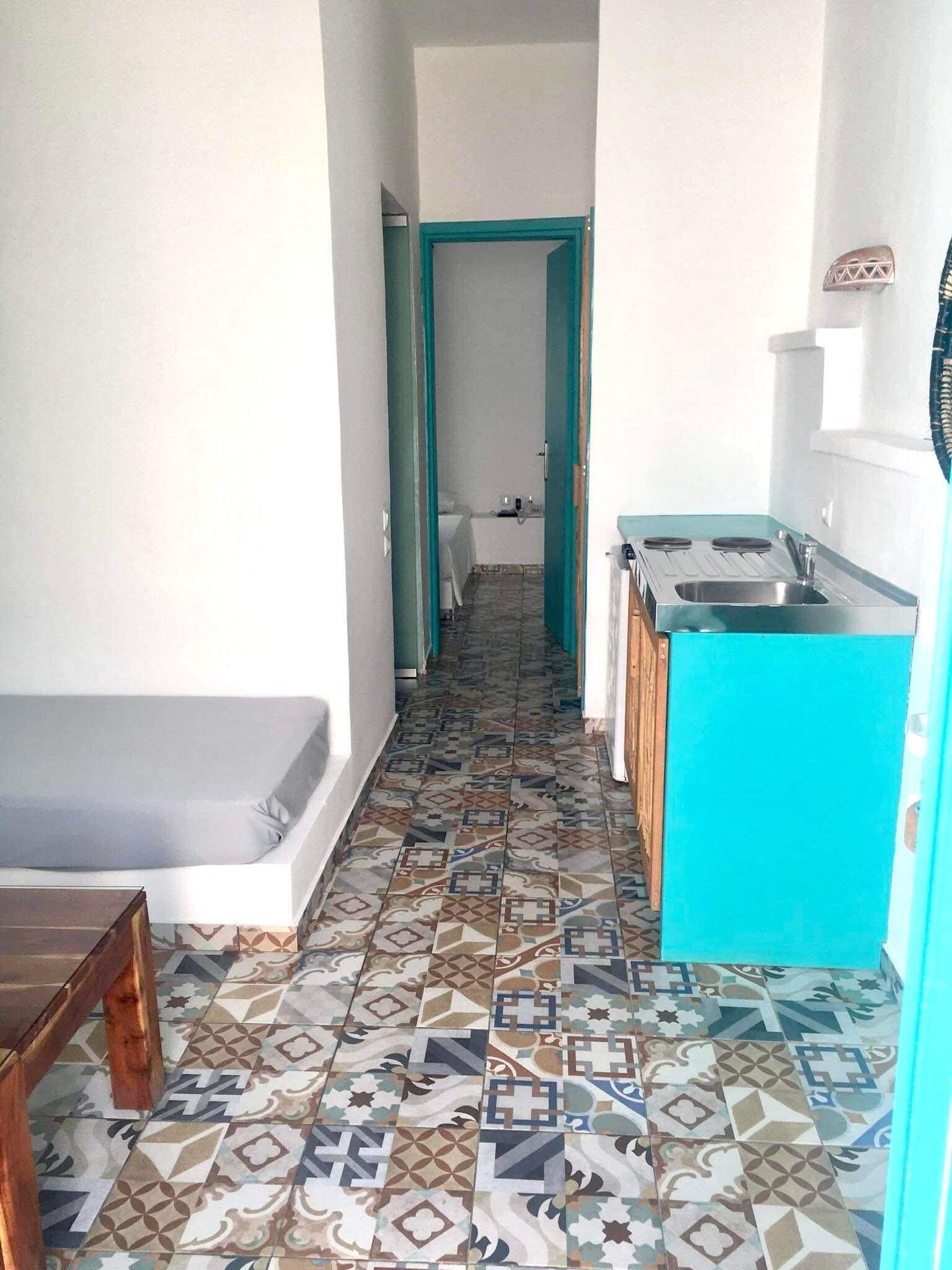 A narrow hallway with a patterned floor leading to a bathroom and a kitchenette area.