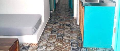 A narrow hallway with a patterned floor leading to a bathroom and a kitchenette area.