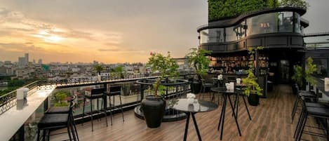A rooftop bar with outdoor seating, a city view, and a curved glass structure.