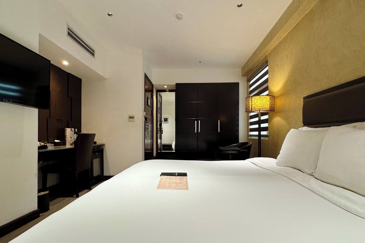 Une chambre d’hôtel avec un grand lit, un bureau, une chaise, une armoire et une lampe de chevet.