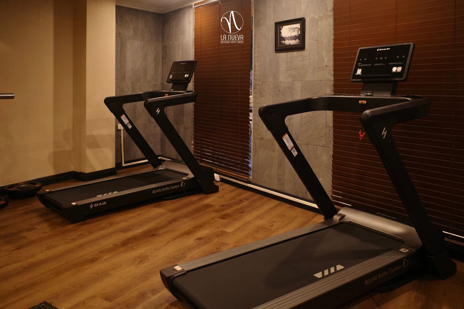A gym with treadmills, a digital kiosk, and a sign for 'LA NUEVA BOUTIQUE HOTEL HANO'.