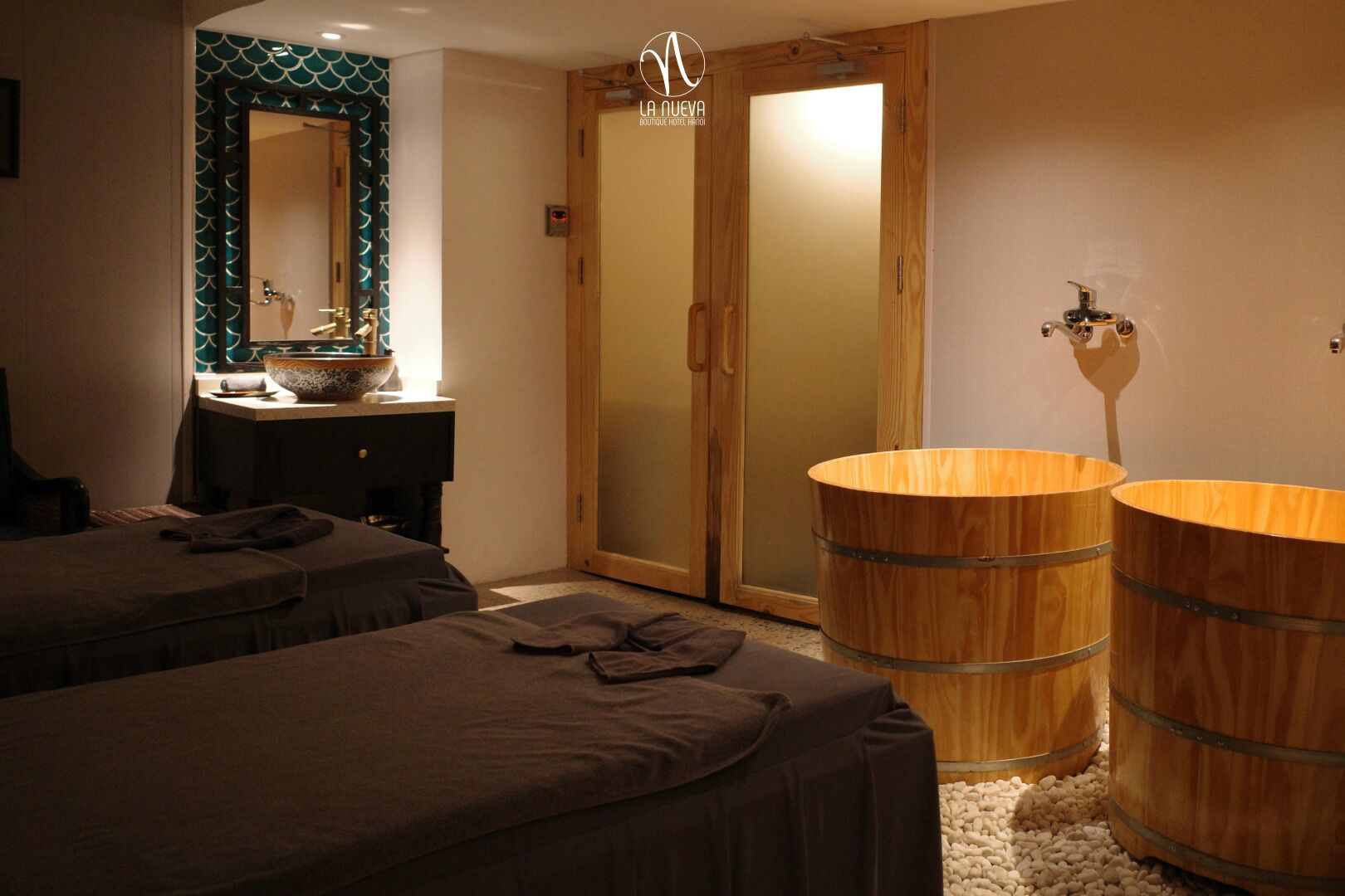 A hotel room with two beds, a wooden vanity with a mirror, a sink, and a wooden barrel tub.