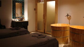 A hotel room with two beds, a wooden vanity with a mirror, a sink, and a wooden barrel tub.