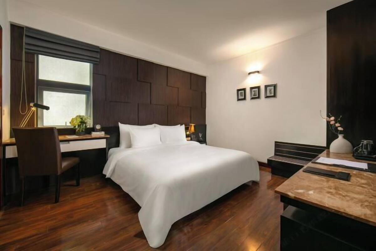 Une chambre d’hôtel moderne, dotée d’un grand lit, d’un bureau, d’une chaise et d’une petite table avec une lampe.