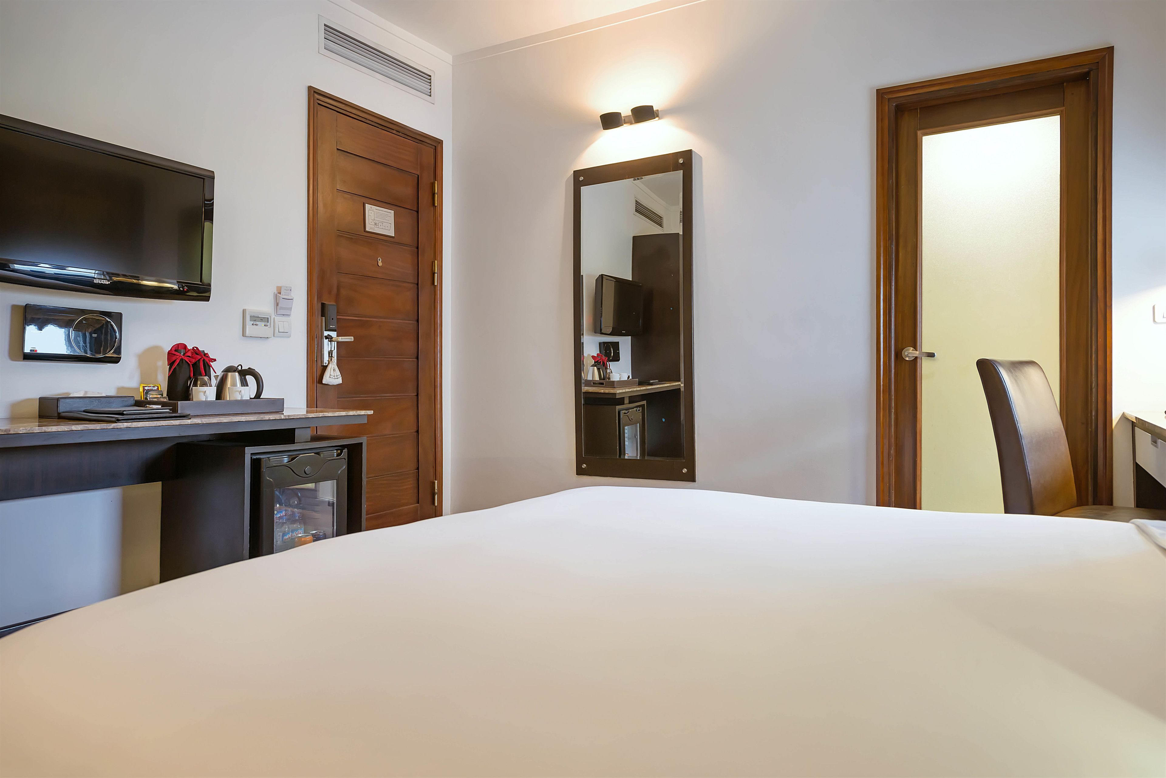 A hotel room with a bed, a desk with a computer, a mirror, and a television.