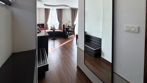 Une chambre d’hôtel moderne dotée d’un grand miroir, d’un petit coin salon avec une table et des chaises, et offrant une vue sur la ville grâce à de grandes fenêtres.