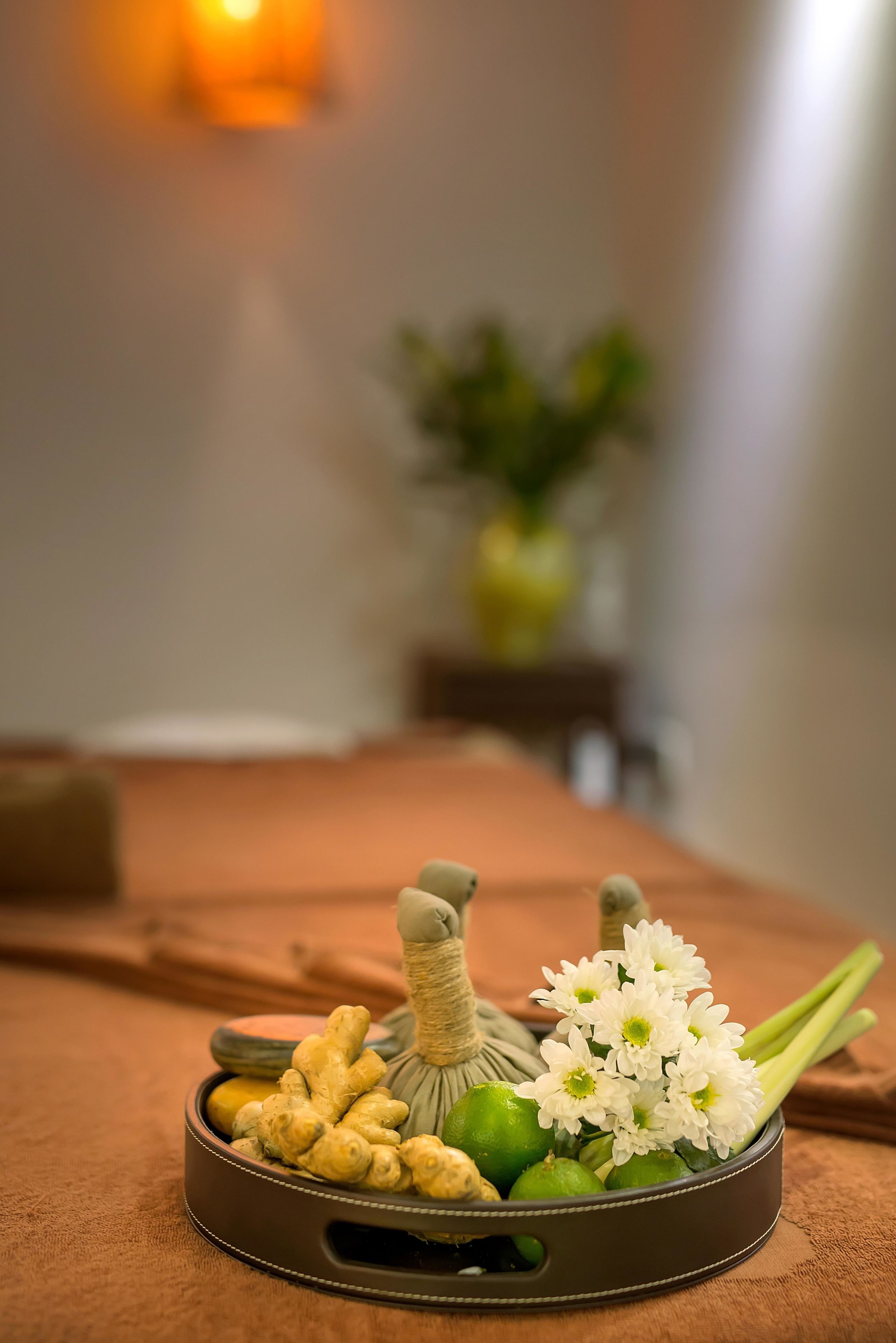 Un plateau contenant du gingembre, du thé vert et des fleurs blanches, posé sur une table marron dans une pièce dont l’arrière-plan est flou.