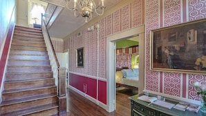 Una escalera de madera conduce a una habitación con papel tapiz estampado y un cuadro en la pared.