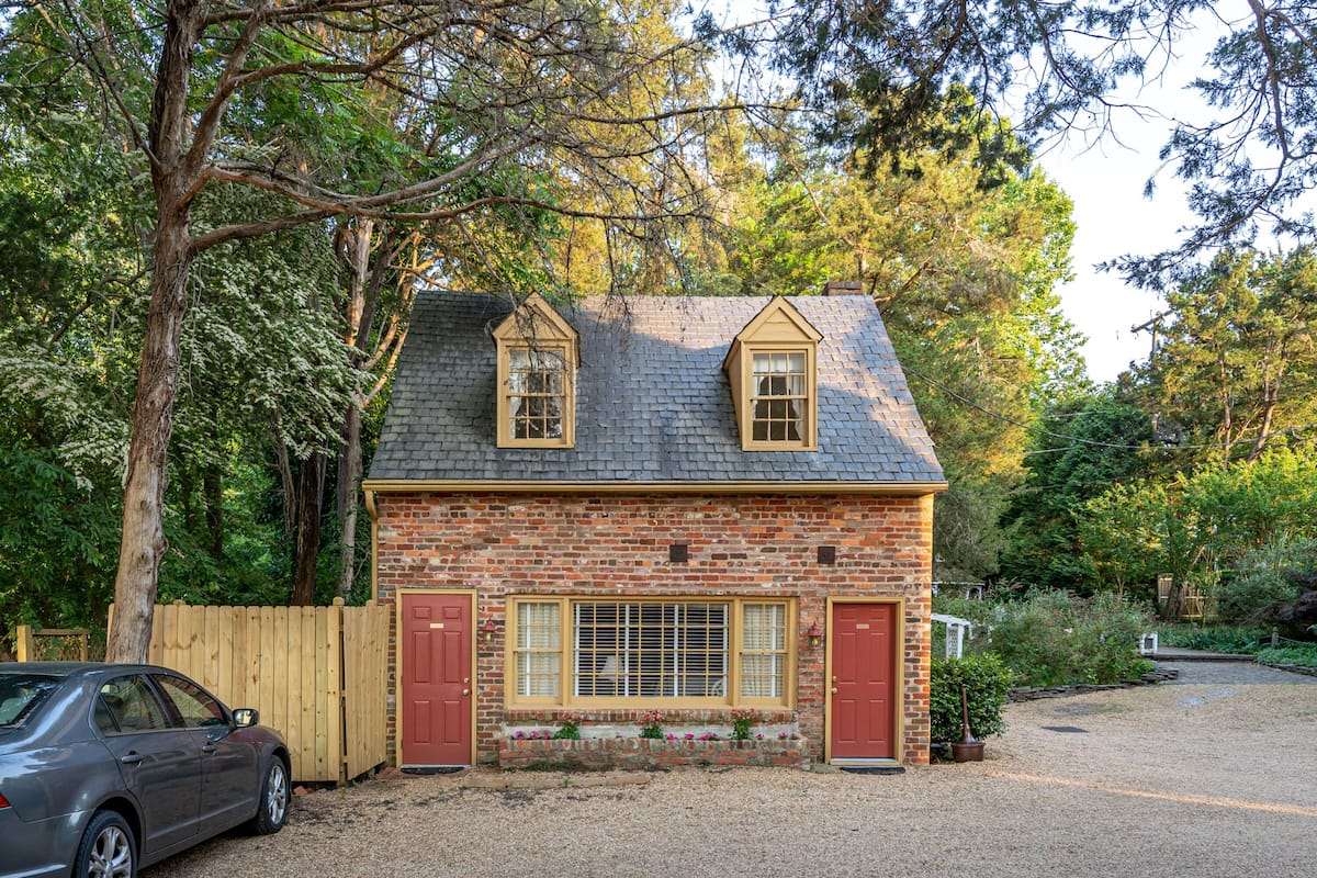 Une petite maison en briques avec un toit en pente, deux fenêtres avec des volets et une clôture en bois.